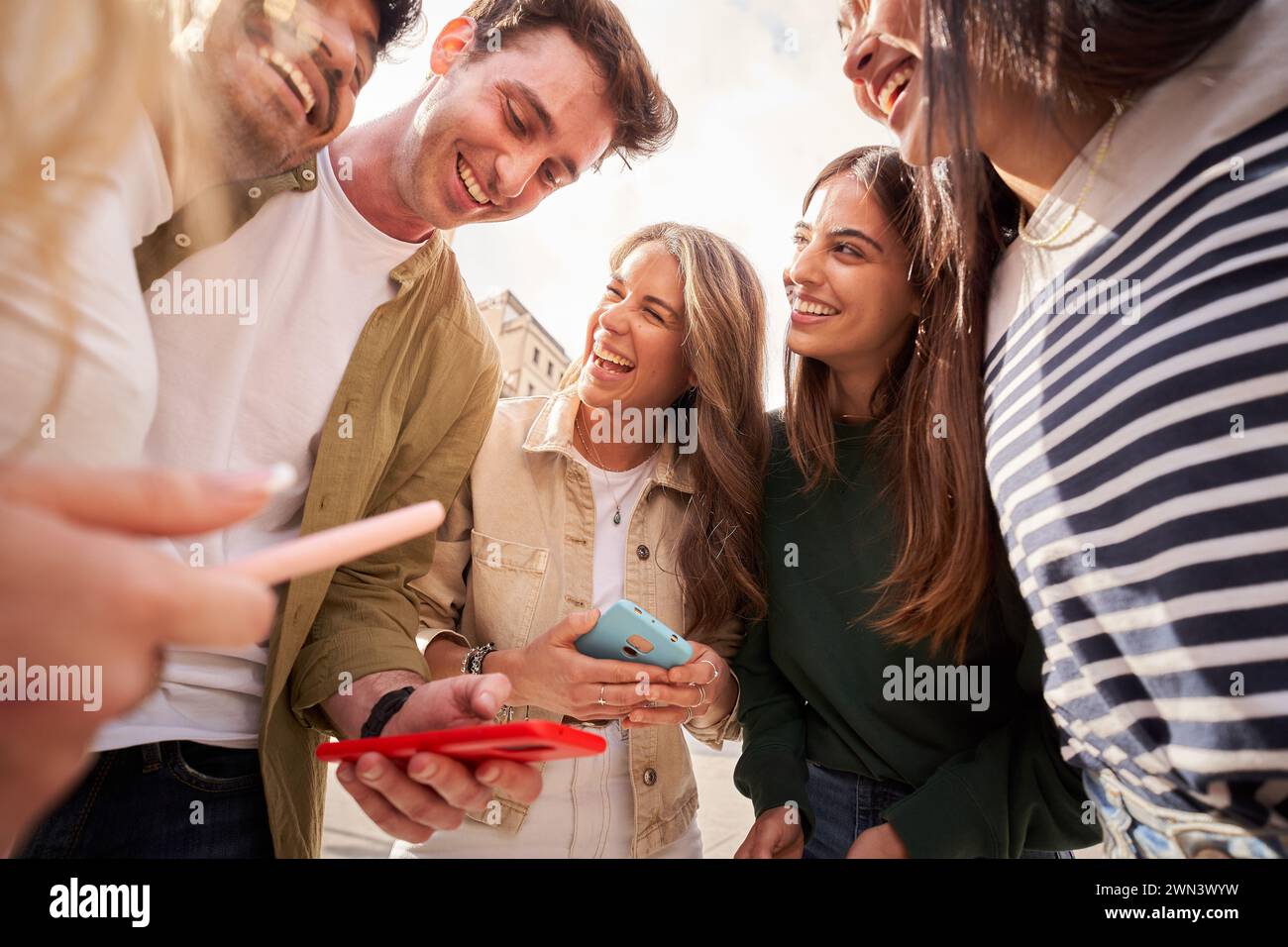 Giovani in cerchio, sorridono mentre condividono un cellulare Foto Stock