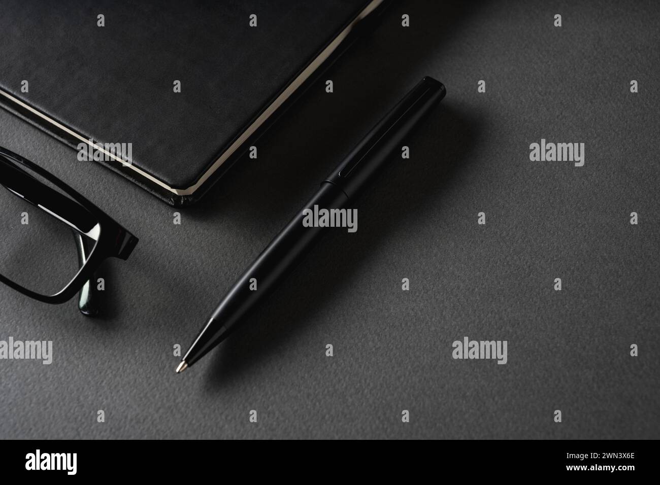 Vista dall'alto della penna a sfera, degli occhiali e del blocco note su un tavolo grigio scuro Foto Stock
