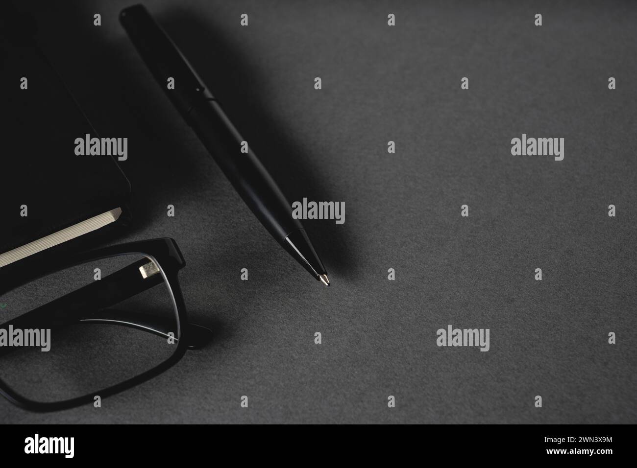 Vista dall'alto della penna a sfera, degli occhiali e del blocco note su un tavolo grigio scuro Foto Stock