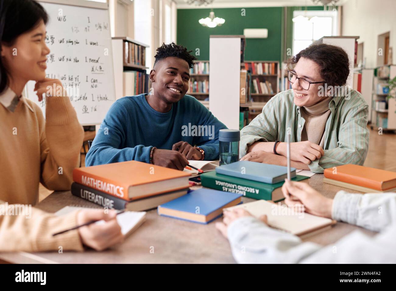 Ritratto di un giovane afro-americano sorridente che si diverte a discutere con un gruppo multietnico di studenti nella biblioteca universitaria Foto Stock