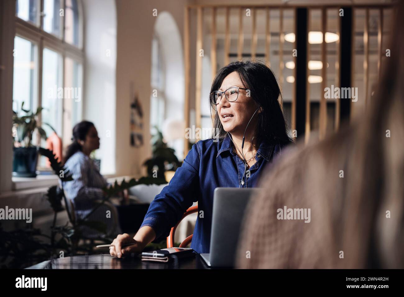 Donna d'affari che parla con cuffie cablate in un ufficio di coworking Foto Stock