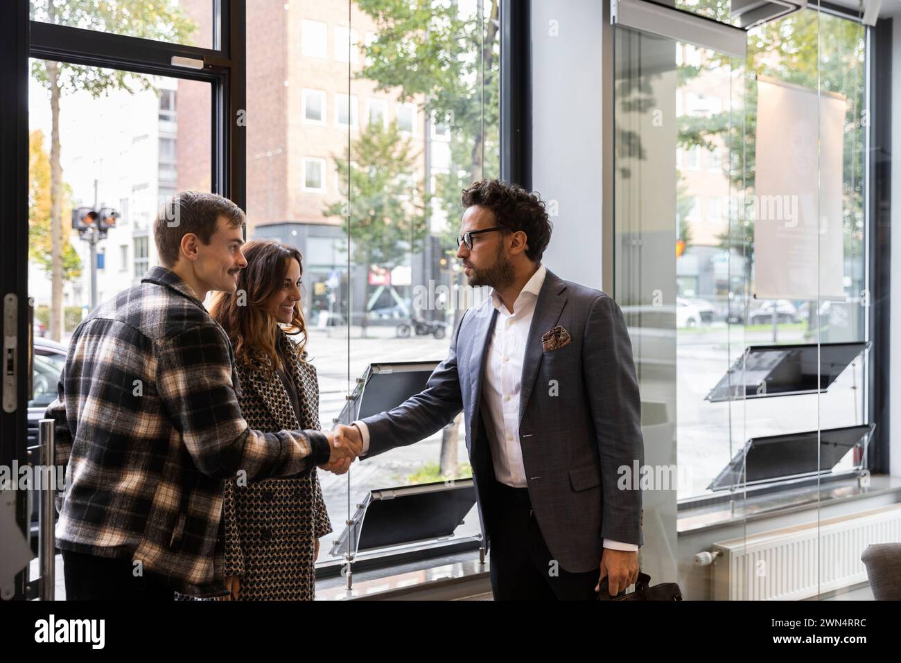 Coppia felice che stringe la mano con un agente immobiliare all'entrata dell'ufficio Foto Stock
