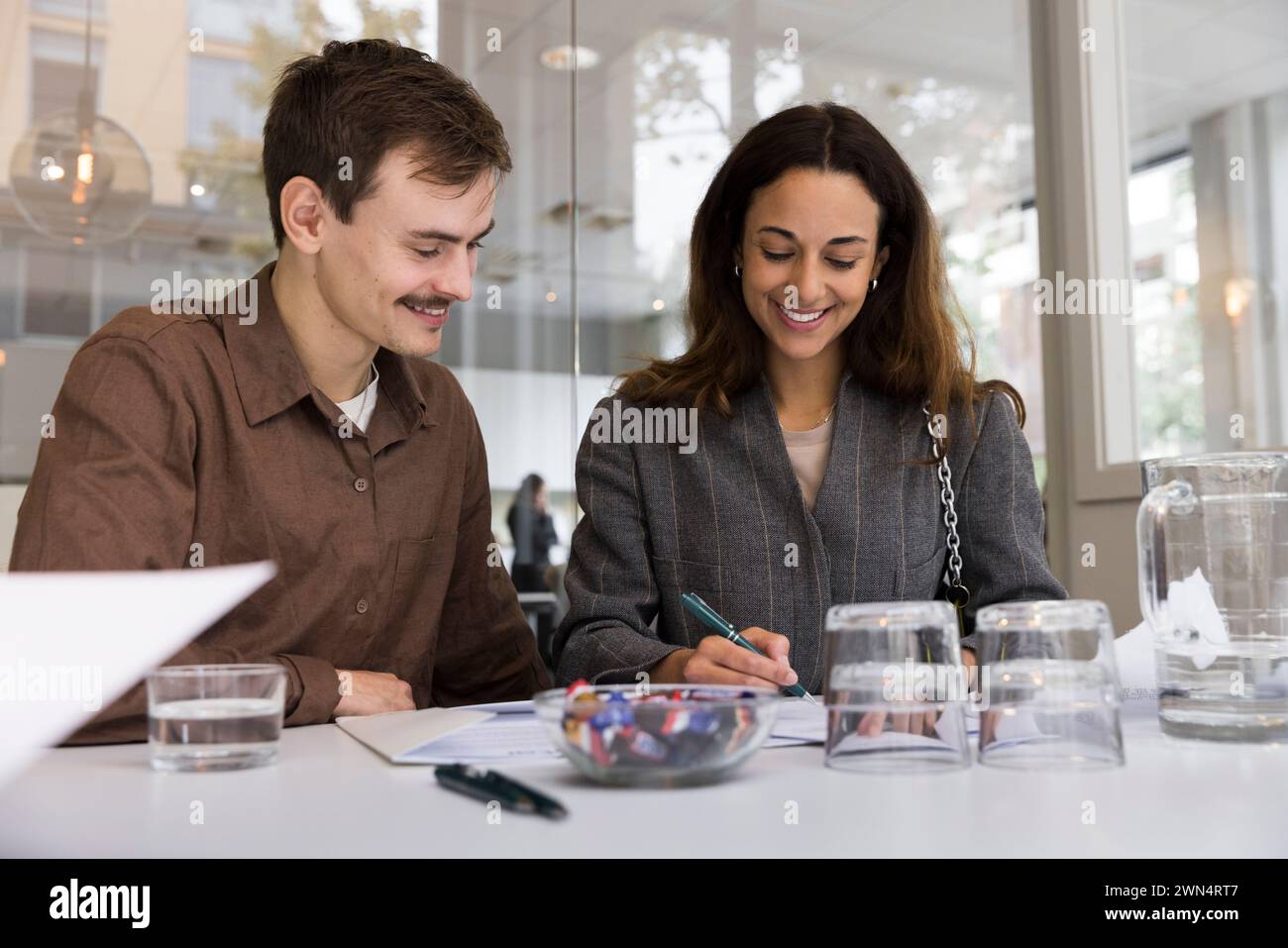 Uomo che guarda una donna sorridente che firma un accordo alla scrivania dell'ufficio immobiliare Foto Stock