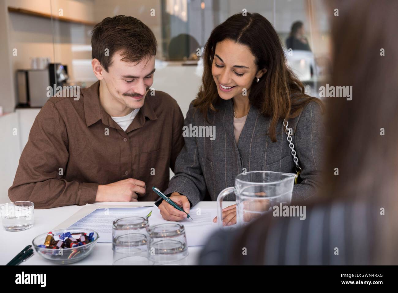 Coppia felice sorridente mentre firma un accordo alla scrivania dell'ufficio immobiliare Foto Stock