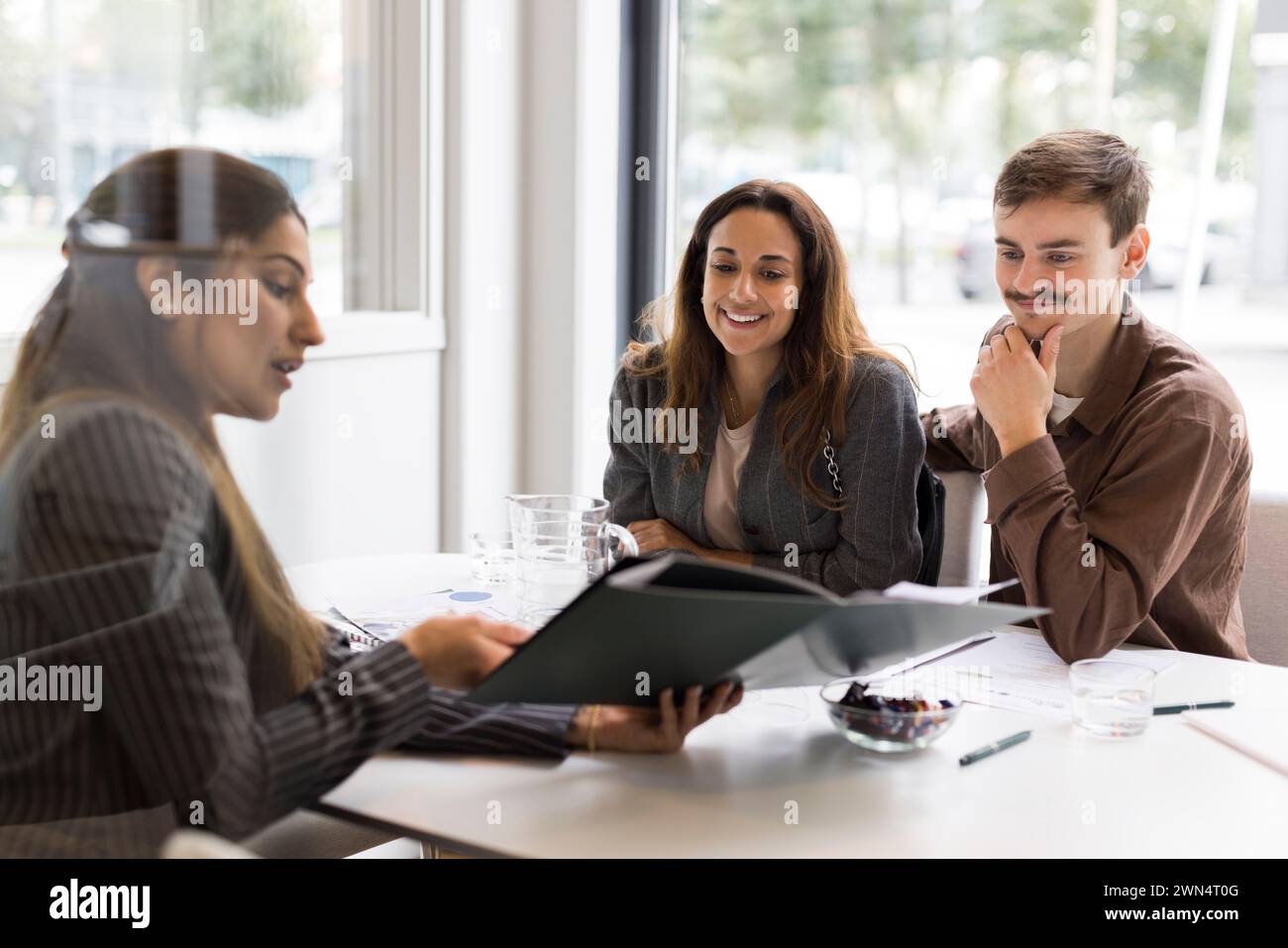 Agente immobiliare donna che mostra la planimetria ai clienti sorridenti in ufficio Foto Stock
