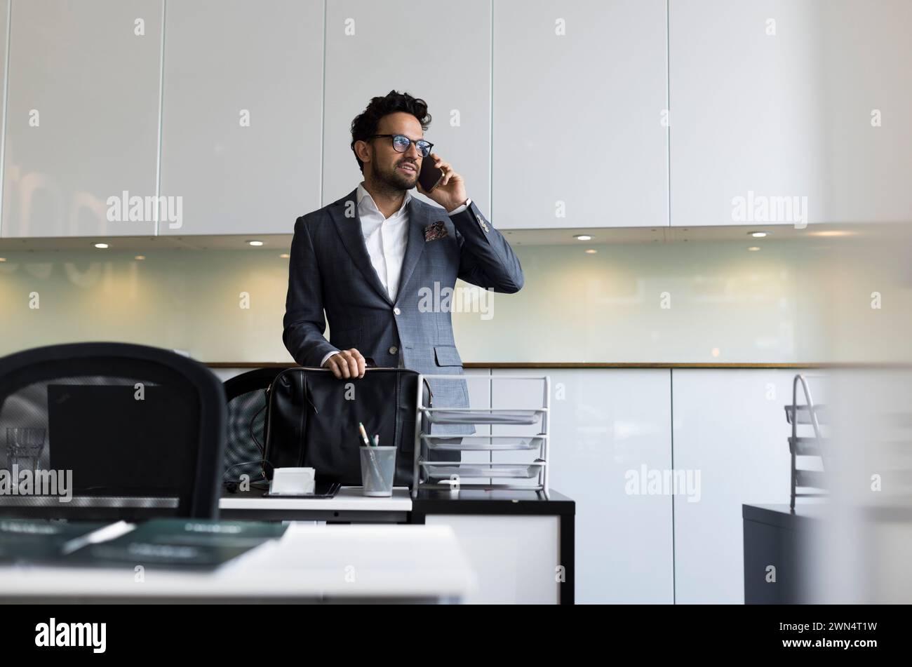 Agente immobiliare maschile che parla con uno smartphone alla scrivania in ufficio Foto Stock