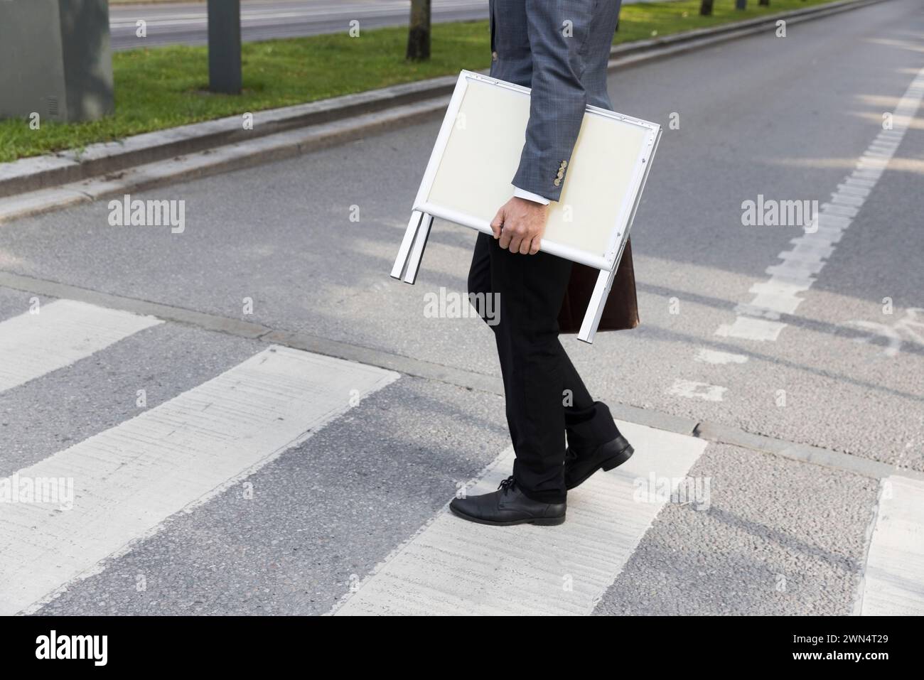Sezione bassa dell'agente immobiliare che porta un cartello mentre attraversa la strada Foto Stock