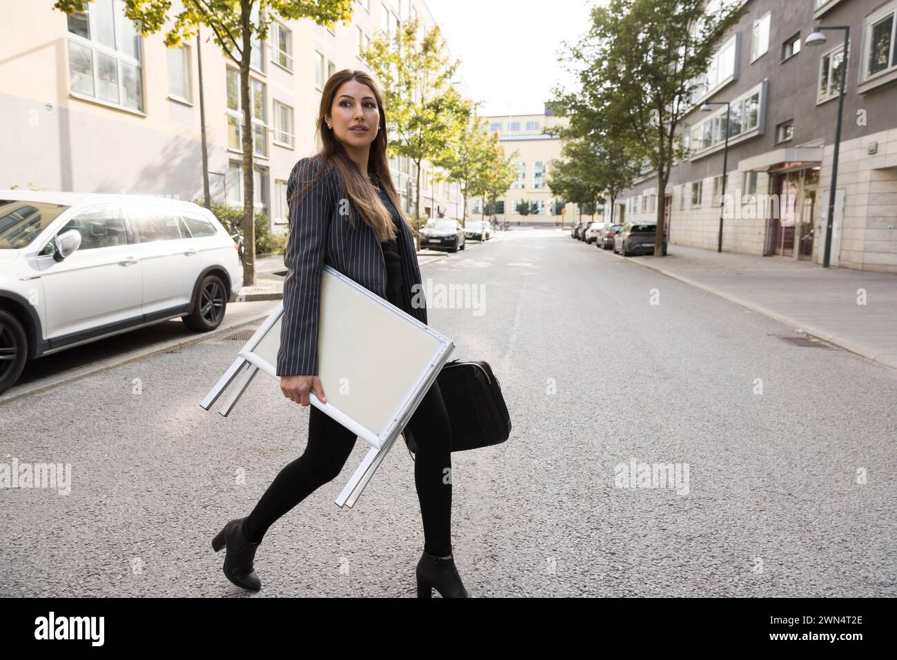 Agente immobiliare donna che porta un cartello mentre attraversa la strada in città Foto Stock
