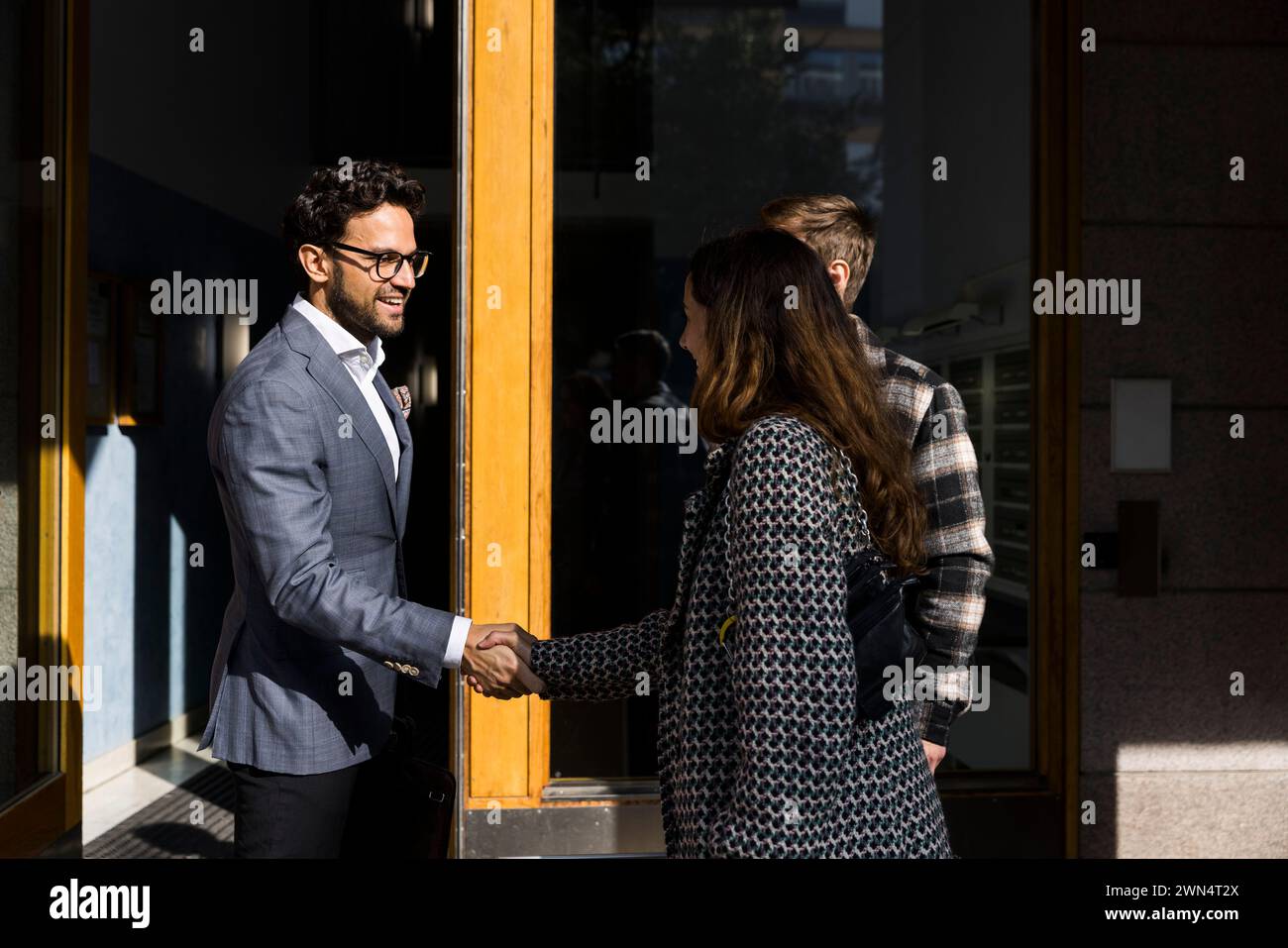 Agente immobiliare maschile che stringe la mano con i clienti di fronte all'appartamento Foto Stock
