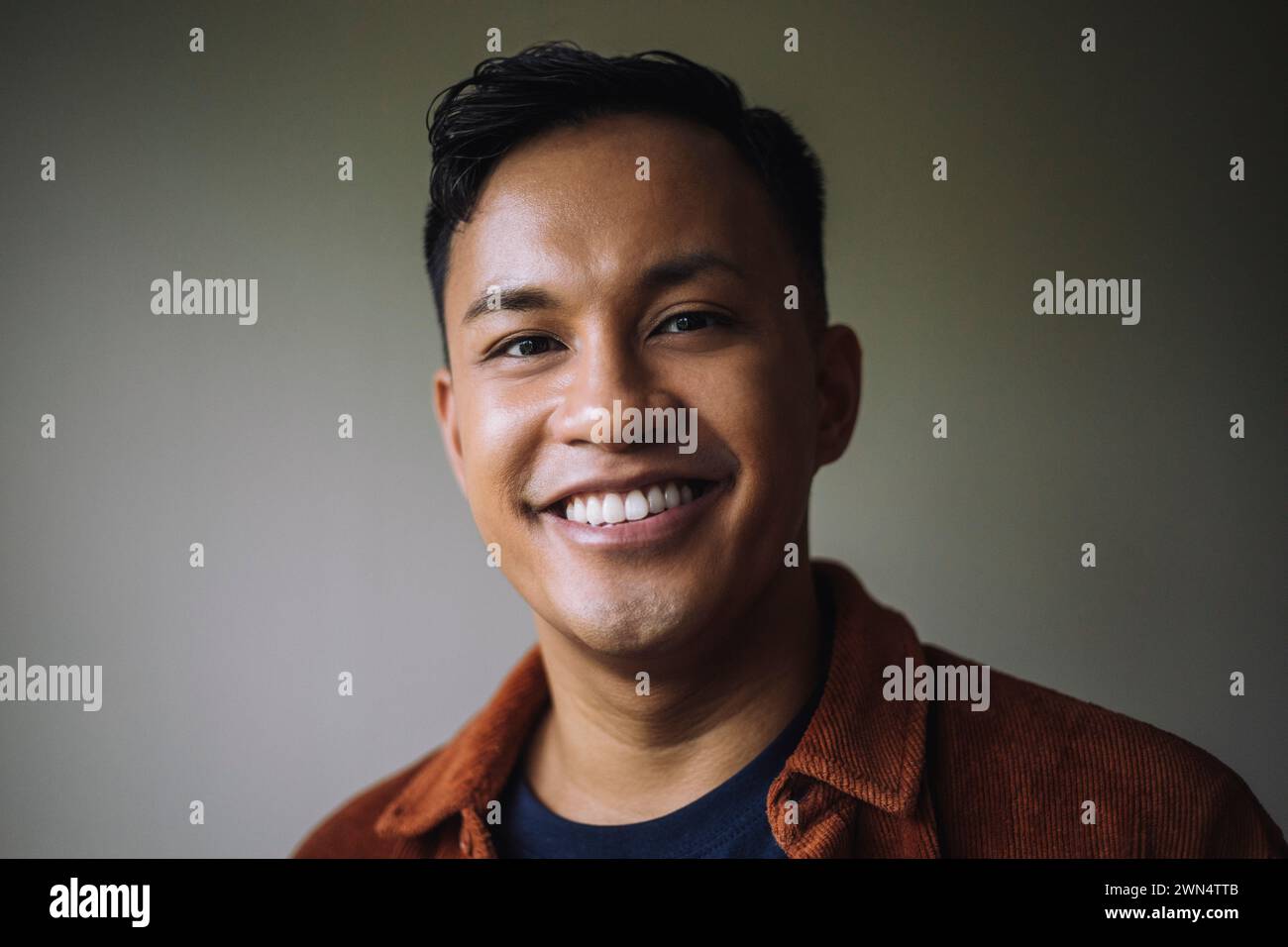 Ritratto di un uomo sorridente davanti al muro a casa Foto Stock