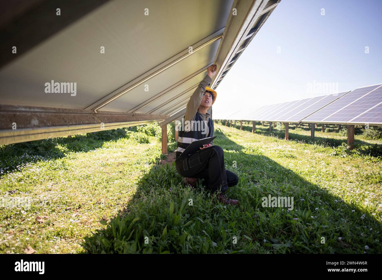 Ingegnere donna che ripara i pannelli solari mentre si inginocchia sull'erba della centrale elettrica Foto Stock