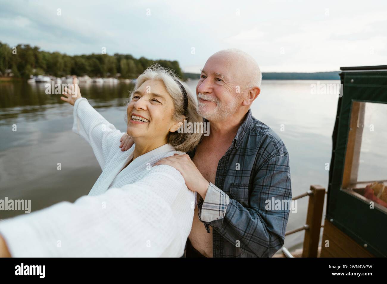 Uomo anziano con le mani sulla spalla di una donna felice sulla casa galleggiante vicino al fiume Foto Stock