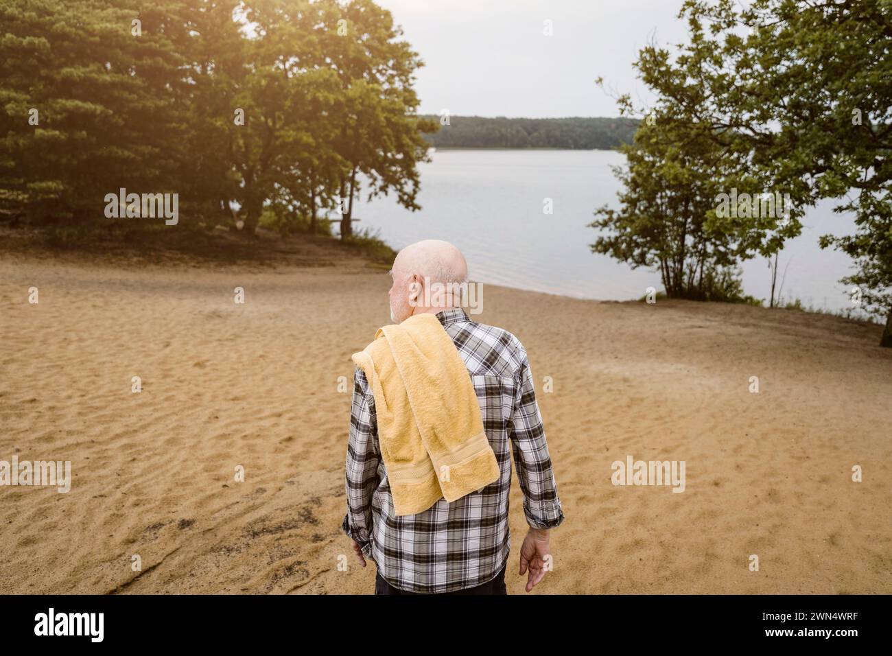 Vista posteriore dell'anziano con un asciugamano sulle spalle che cammina verso il fiume Foto Stock