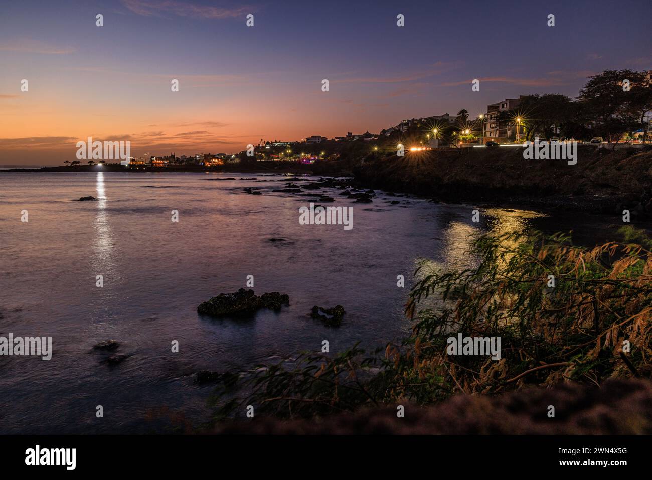 Scena notturna delle luci della città di Praia, capitale di Cabo Verde, riprodotta nelle calme acque di una baia a lunga esposizione Foto Stock