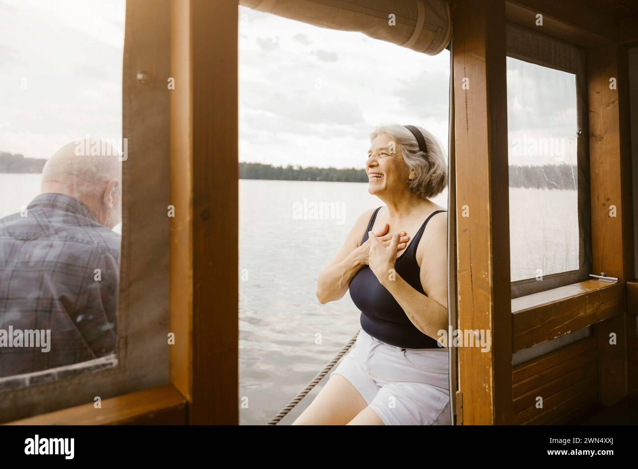 Donna anziana felice con le mani sul petto seduta vicino a un uomo alla casa galleggiante Foto Stock