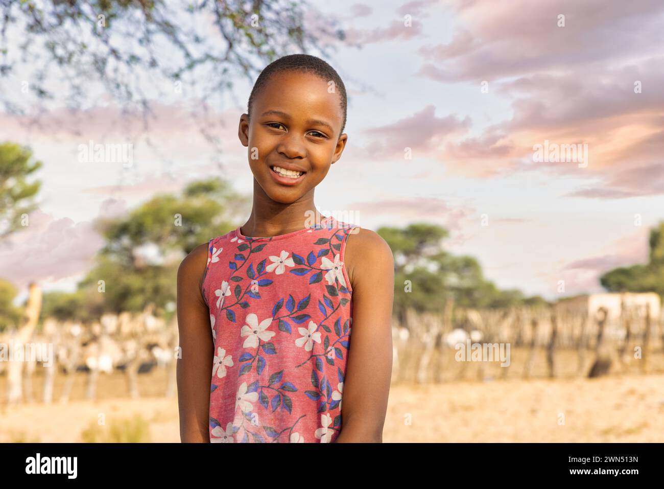 ragazza africana con un grande sorriso di toothy , nel villaggio, in piedi davanti alla penna kraal con piccolo bestiame Foto Stock