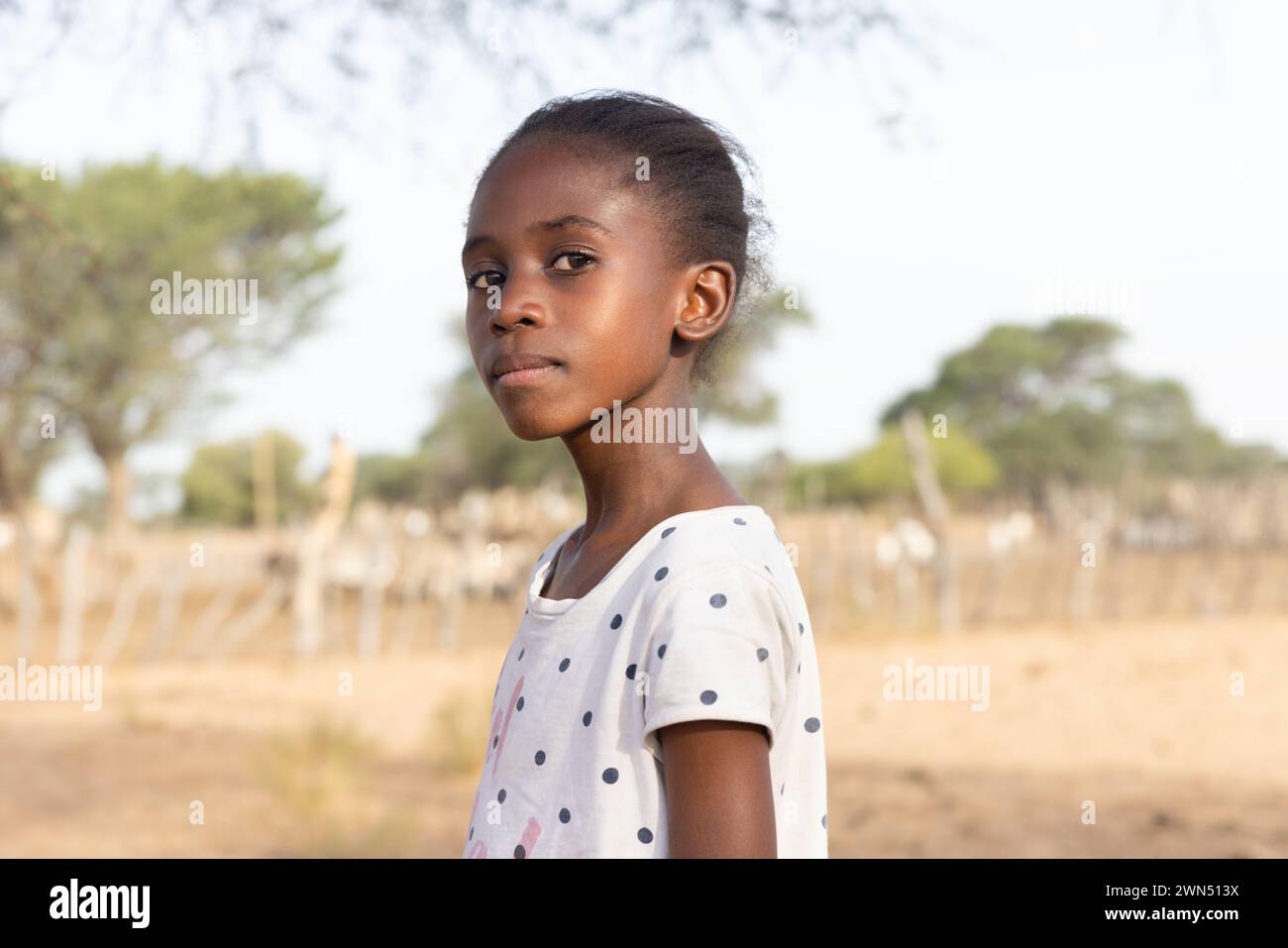ragazza africana con un'espressione orgogliosa , nel villaggio, in piedi di fronte al kraal con piccoli animali Foto Stock