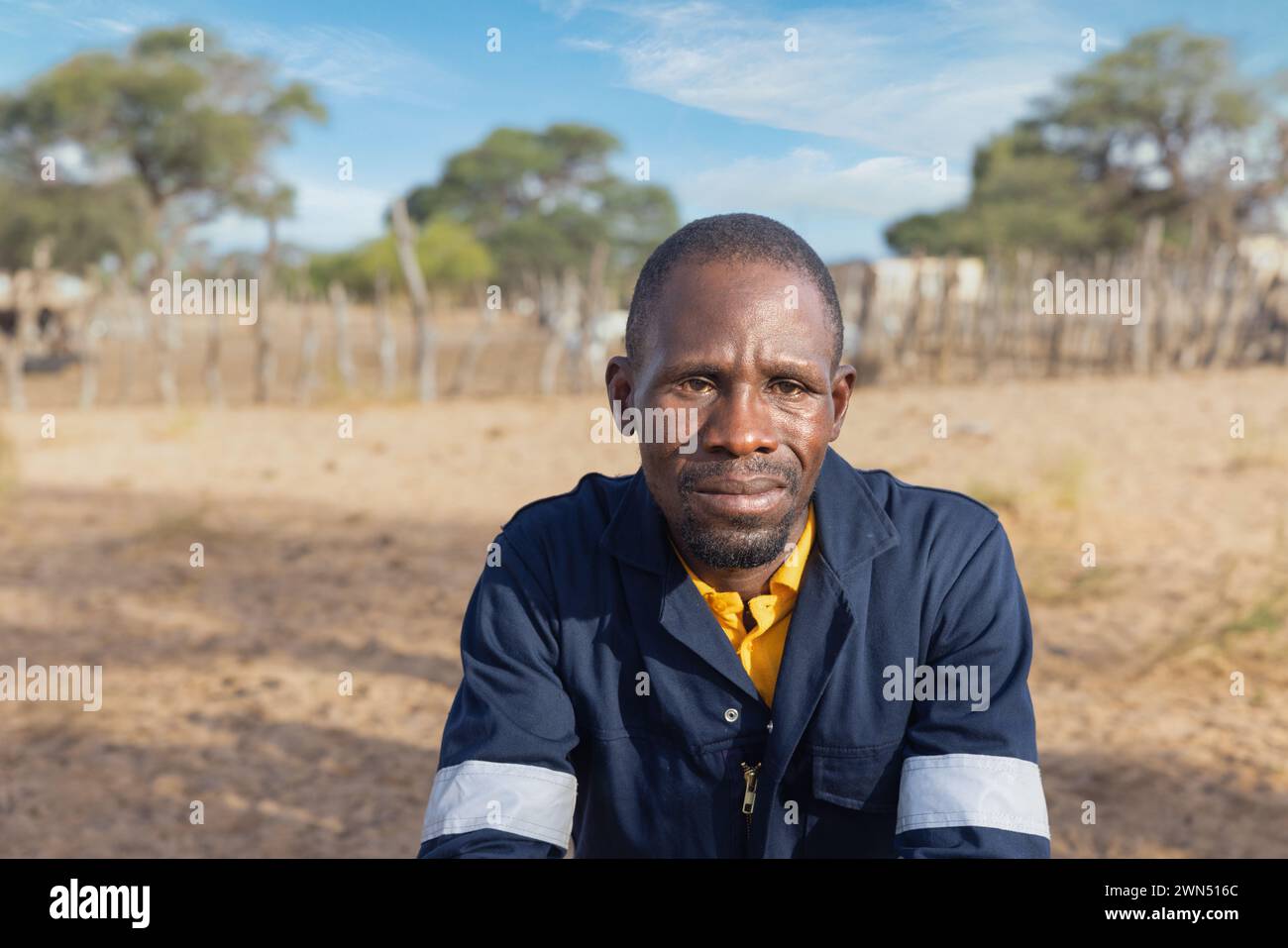 uomo africano in abbigliamento da lavoro , nel villaggio, in piedi di fronte al kraal con piccoli animali Foto Stock