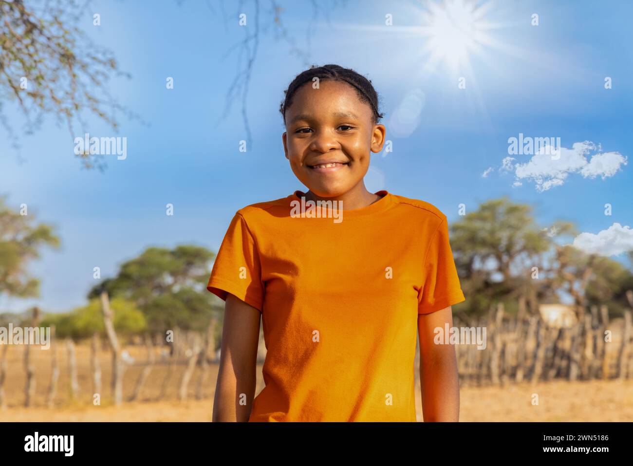 ragazza africana con un grande sorriso di toothy , nel villaggio, in piedi davanti alla penna kraal con piccolo bestiame, in una giornata di sole Foto Stock