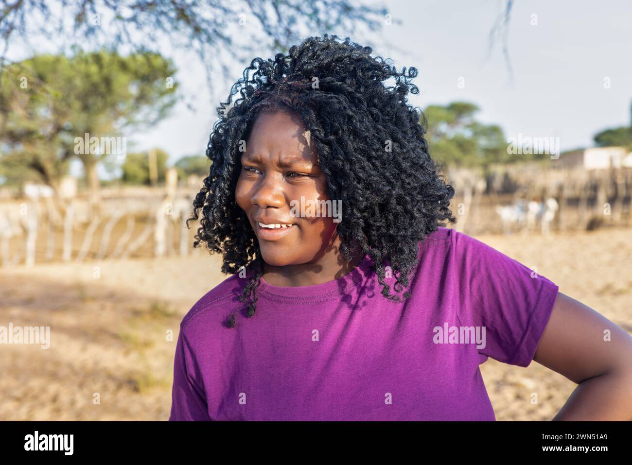 donna africana con trecce , nel villaggio, in piedi di fronte al kraal con piccolo bestiame Foto Stock