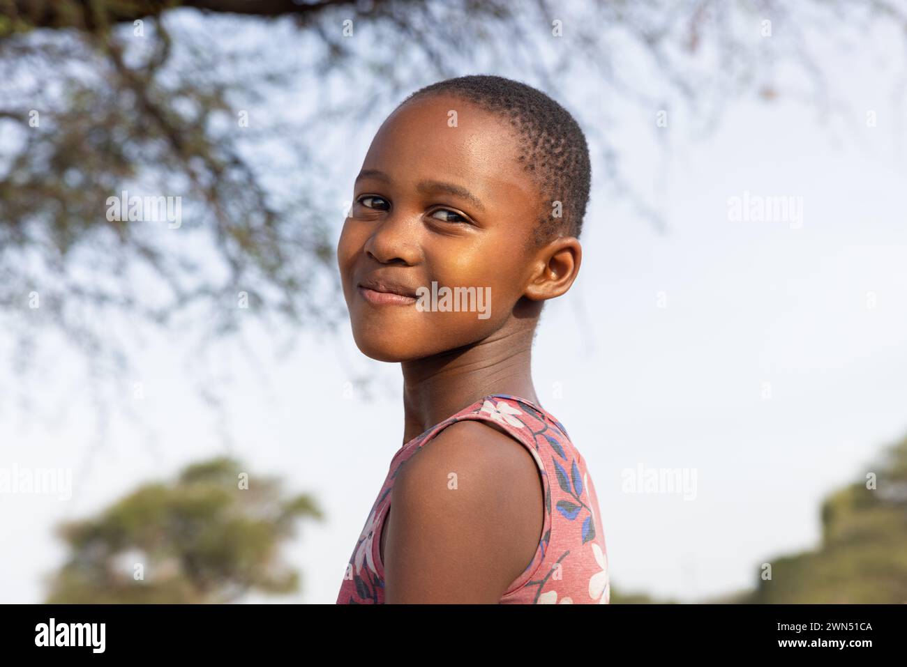 ragazza africana con un grande sorriso di toothy , nel villaggio, in piedi nel cortile accanto ad un albero Foto Stock