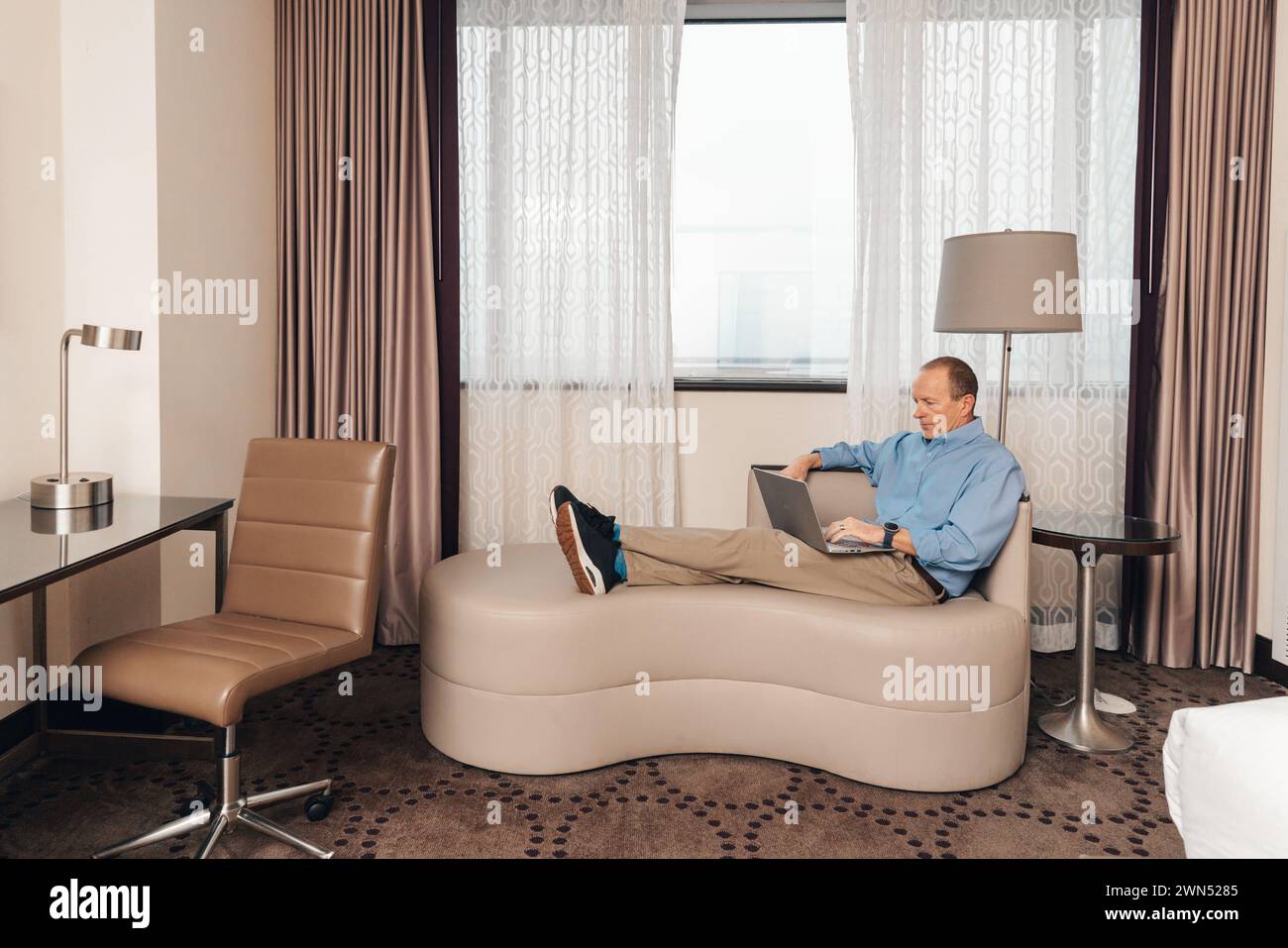 uomo in un abbigliamento casual per lavoro che lavora su un computer portatile in una camera d'hotel Foto Stock