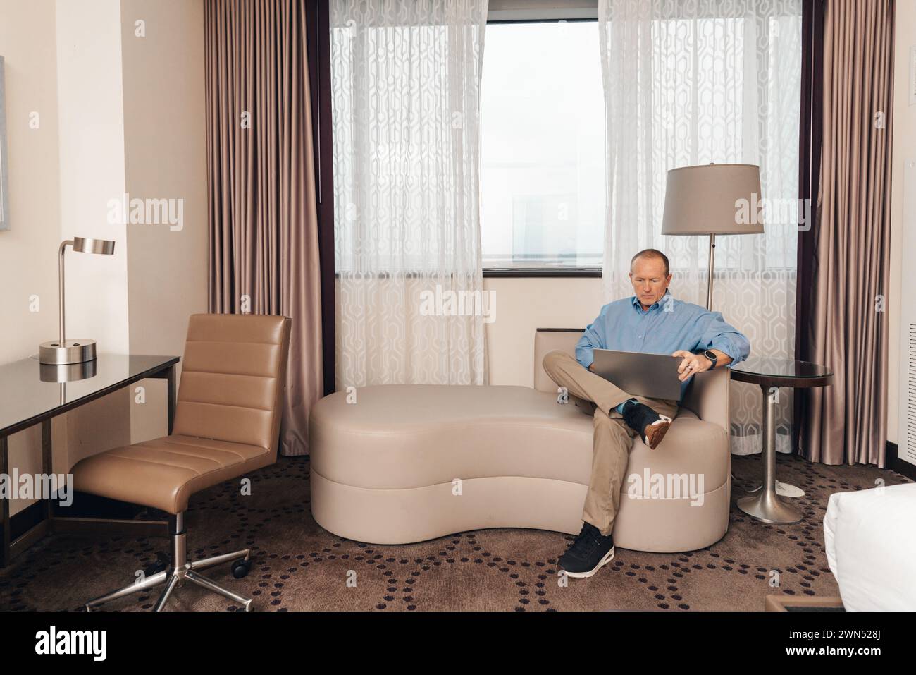 uomo in un abbigliamento casual per lavoro che lavora su un computer portatile in una camera d'hotel Foto Stock