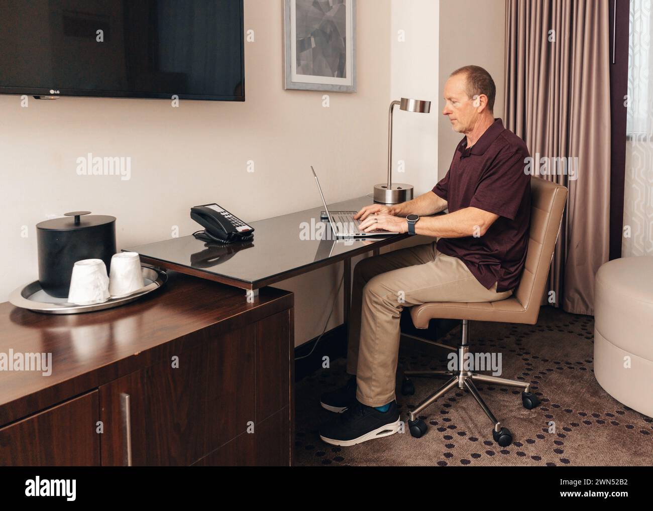 uomo in un abbigliamento casual per lavoro che lavora su un computer portatile in una camera d'hotel Foto Stock