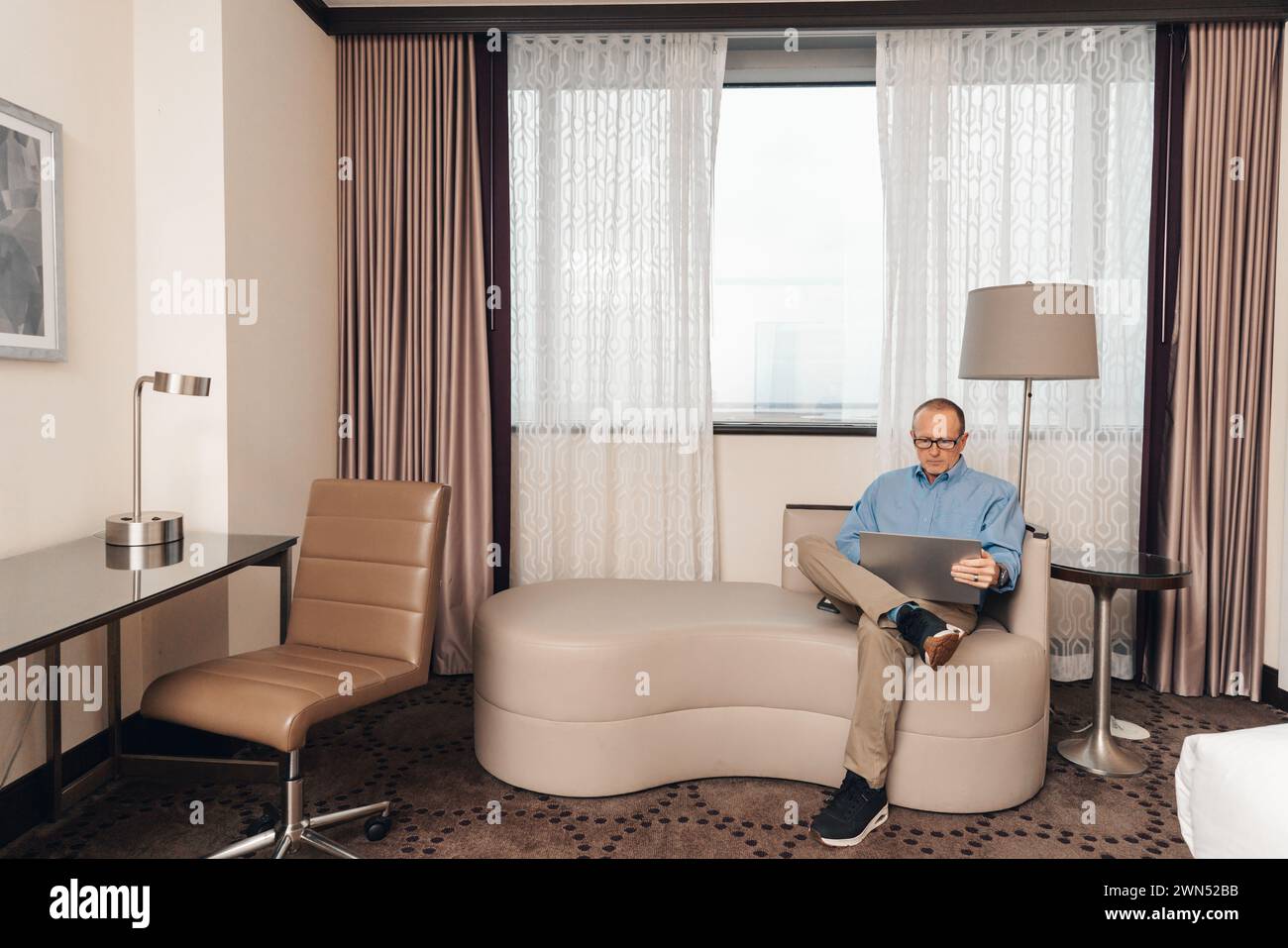 uomo in un abbigliamento casual per lavoro che lavora su un computer portatile in una camera d'hotel Foto Stock