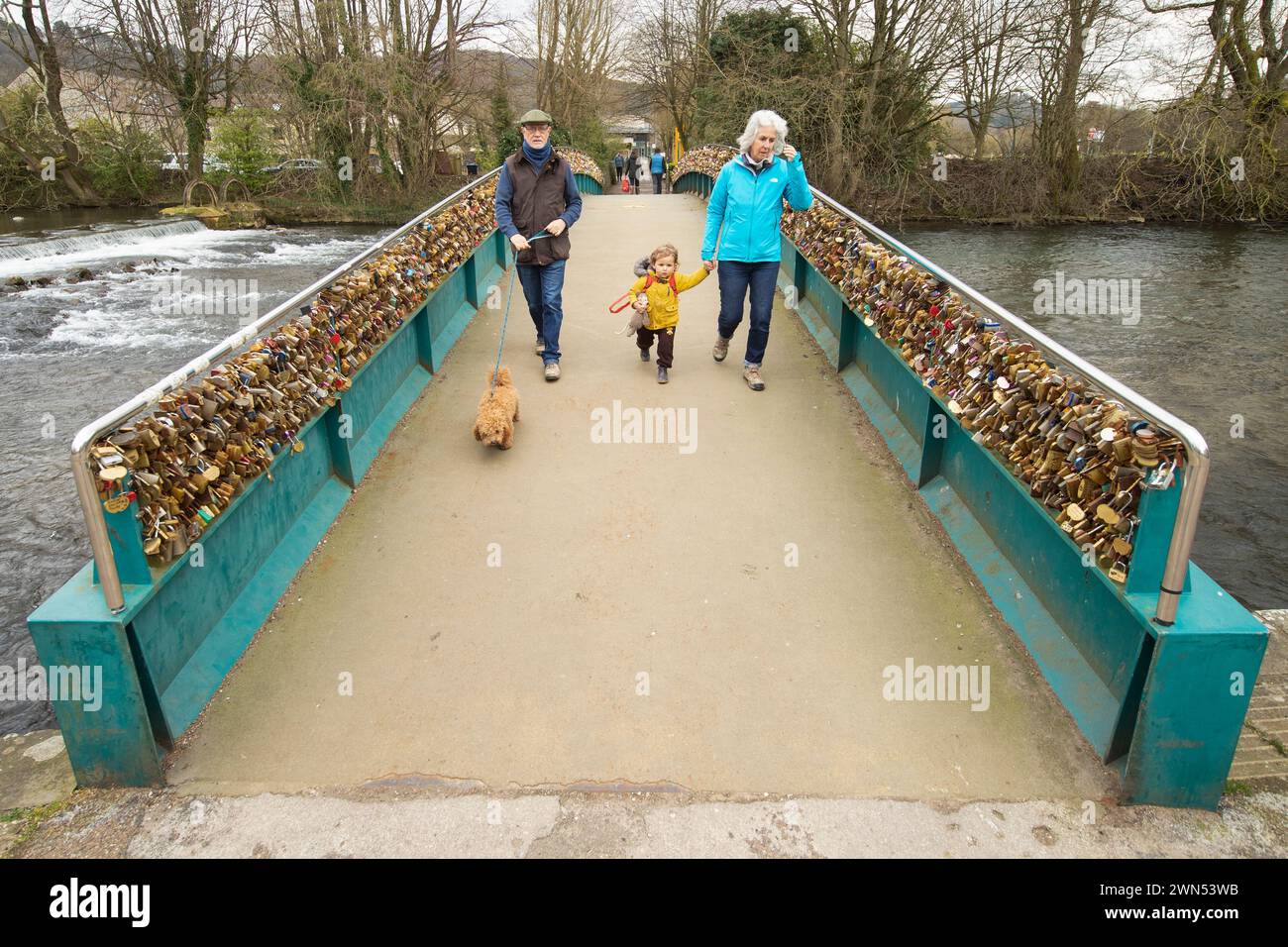 24/03/21 Murdoch, Finley e Mandi Crawford attraversano il ponte pedonale. Il ponte Ôlove lockÕ Weir sul fiume Wye a Bakewell. Prevede di rimuoverlo Foto Stock