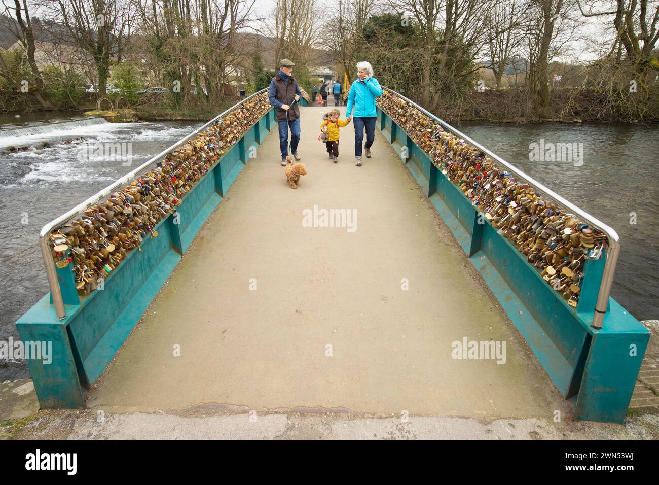 24/03/21 Murdoch, Finley e Mandi Crawford attraversano il ponte pedonale. Il ponte Ôlove lockÕ Weir sul fiume Wye a Bakewell. Prevede di rimuoverlo Foto Stock