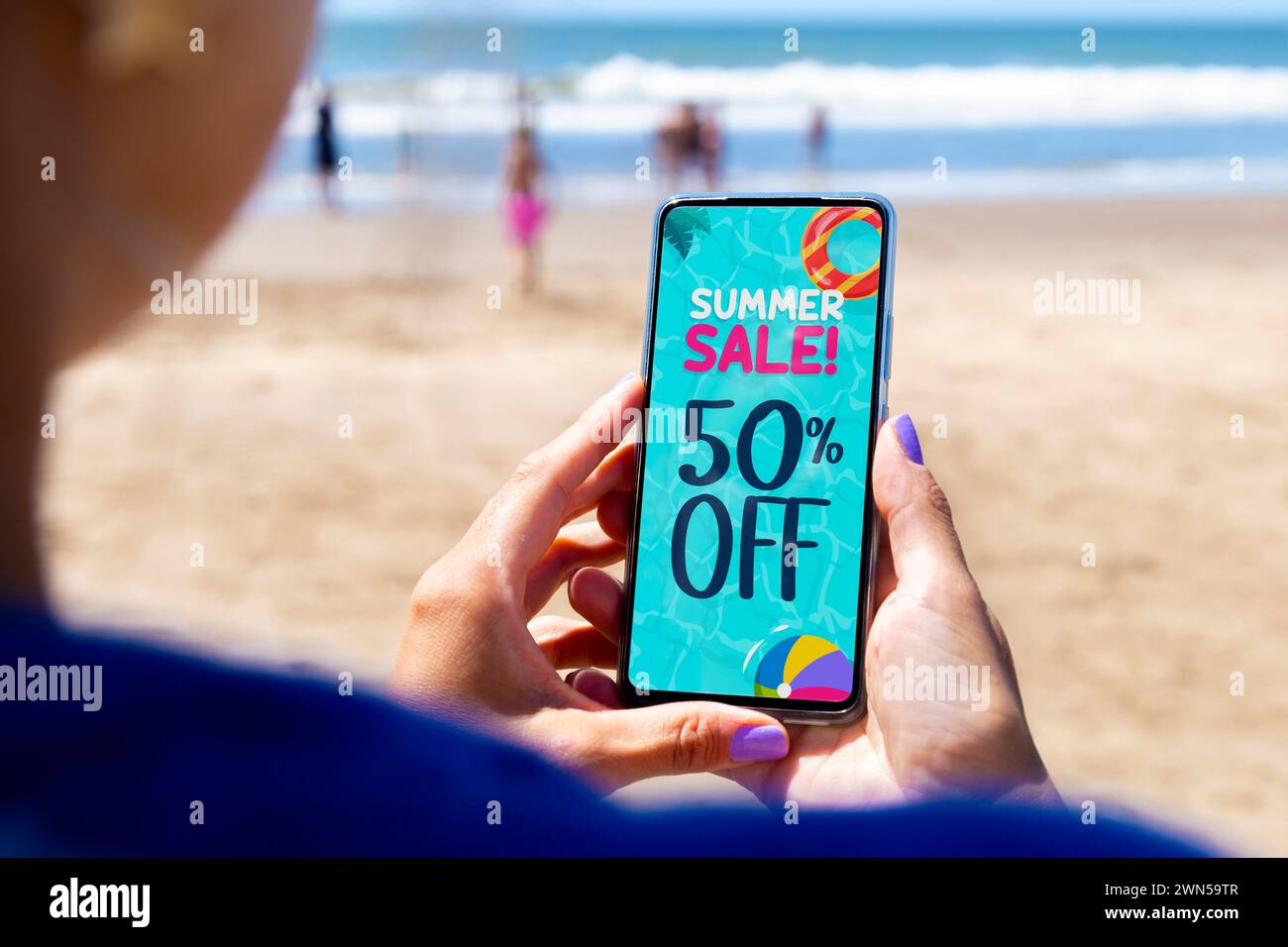 sconto del 50% sui saldi estivi. Donna in spiaggia con un telefono cellulare che mostra un'offerta o un coupon sullo schermo. Foto Stock