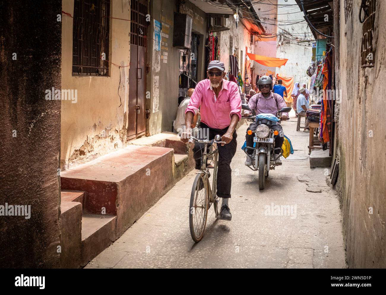 Un uomo in bicicletta e un uomo in moto in un vicolo di Stone Town, Zanzibar, Tanzania Foto Stock