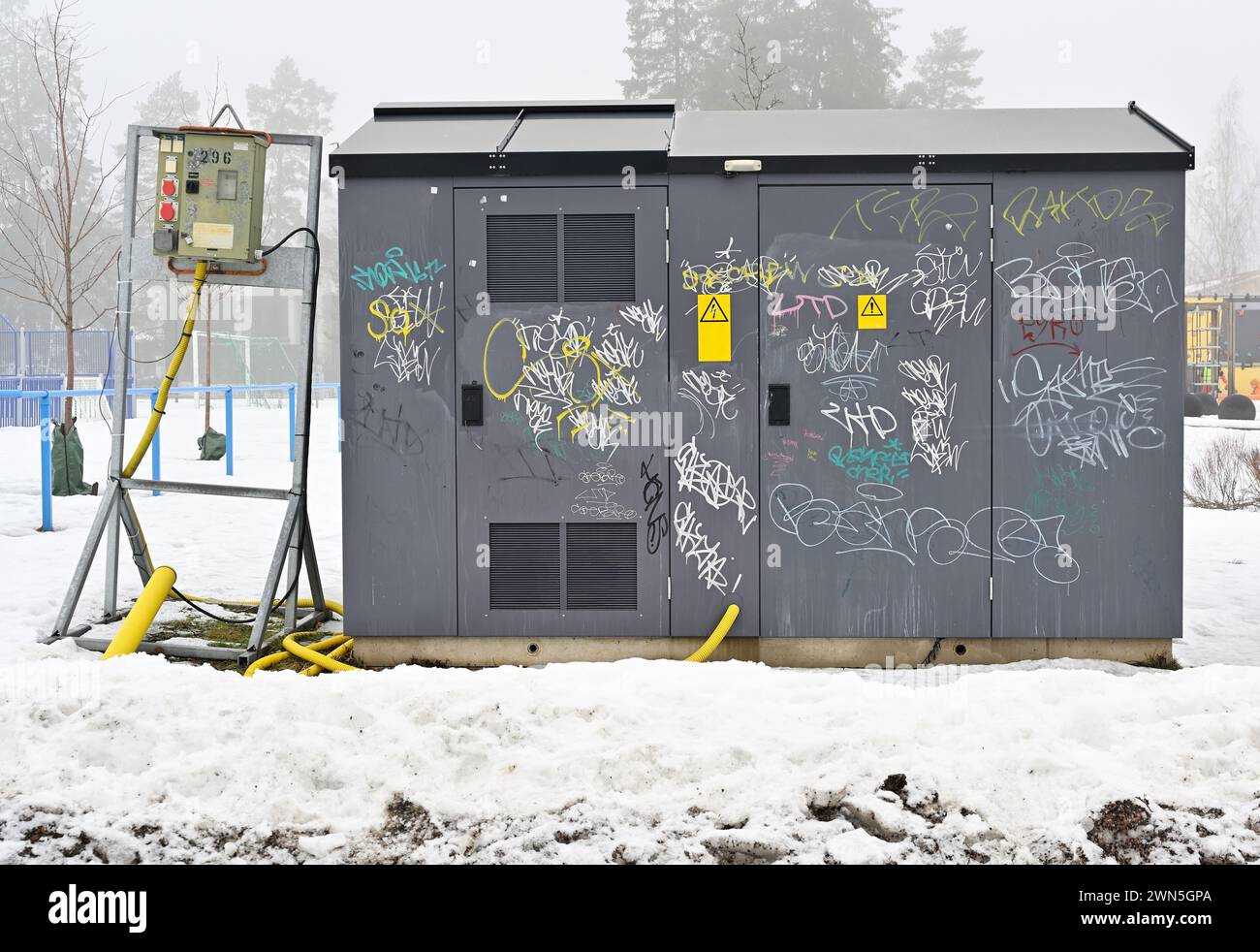 Una scatola di alimentazione elettrica è coperta da varie etichette graffiti, in un paesaggio innevato con nebbia sullo sfondo Foto Stock