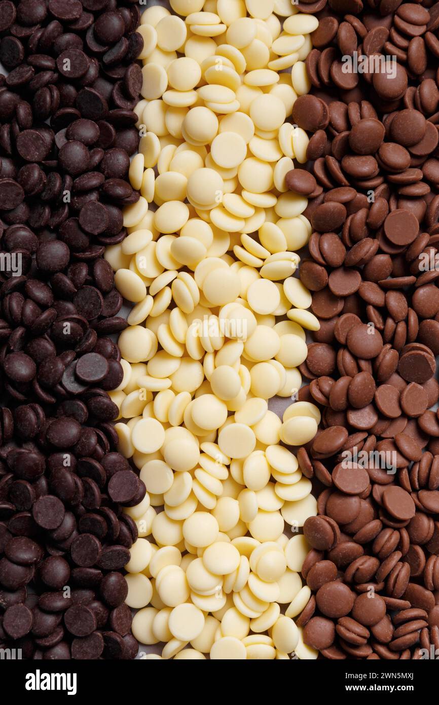 Gocce di cioccolato fondente, bianco e medio per preparare cioccolato, caramelle e torte come sfondo. Concetto di dolciumi al cioccolato temperato. Cioccolato Foto Stock