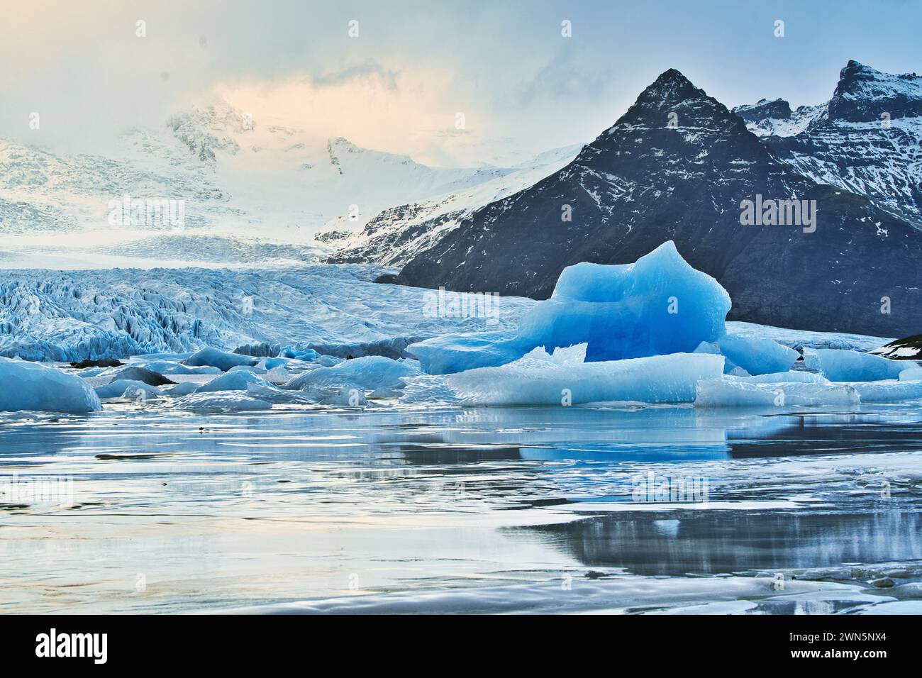 Iceberg in un lago glaciale in Islanda con le montagne sullo sfondo e il ghiacciaio che scende dalle colline fino all'acqua. Foto Stock
