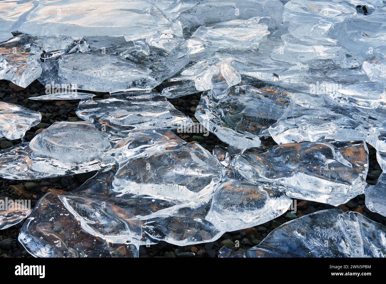 Ghiaccio ghiacciato sulla riva del lago che si sovrappone per formare una scena di riflessi e forme di ghiaccio. Foto Stock