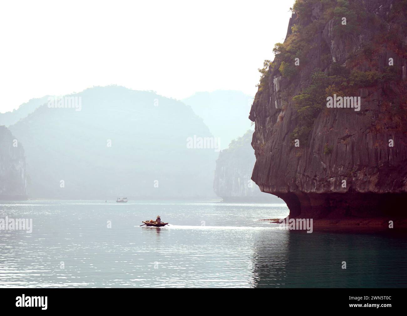 Piccola barca con scogliere calcaree della baia di ha Long sullo sfondo Foto Stock