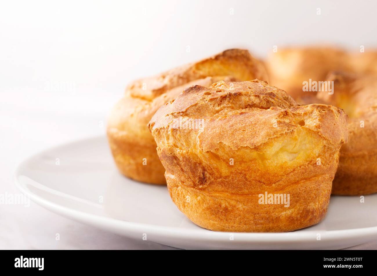 Pover su piastra bianca su sfondo bianco, primo piano. Budino dello Yorkshire come semplice colazione cucinata, cibo gustoso, spuntini leggeri Foto Stock