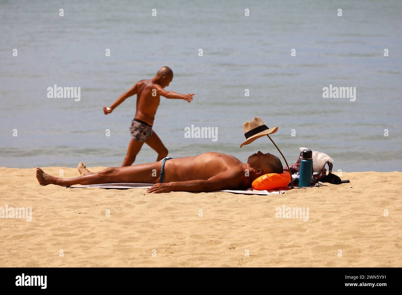 Uomo asiatico abbronzato in tronchi che dorme sulla spiaggia sabbiosa Foto Stock