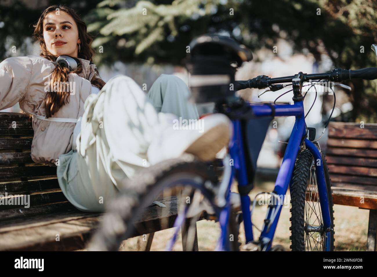 Una giovane donna che fa una pausa su una panchina del parco con la sua bicicletta. Foto Stock