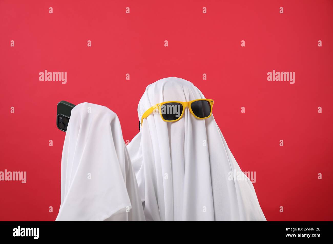 Persona in costume fantasma e occhiali da sole con smartphone su sfondo rosso Foto Stock