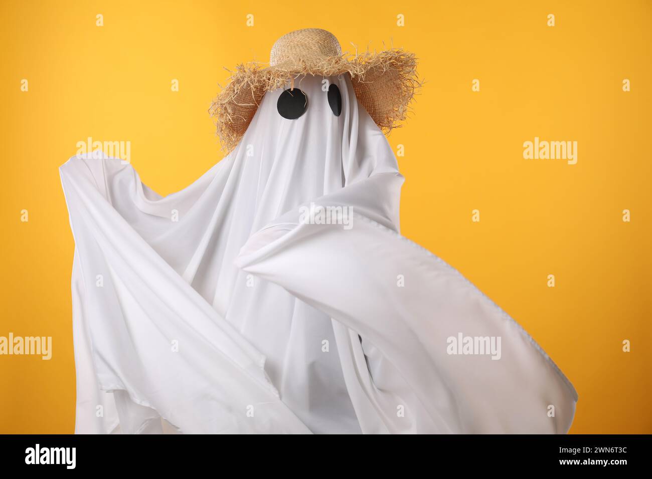 Persona in costume fantasma e cappello di paglia su sfondo giallo Foto Stock
