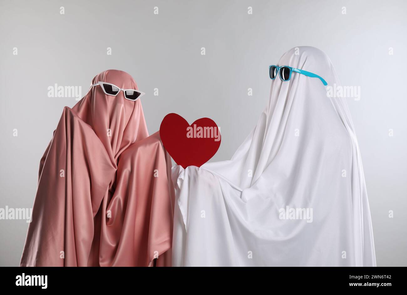 Fantasmi carini. Abbinalo a lenzuola e occhiali da sole a colori con cuore rosso su sfondo grigio chiaro Foto Stock