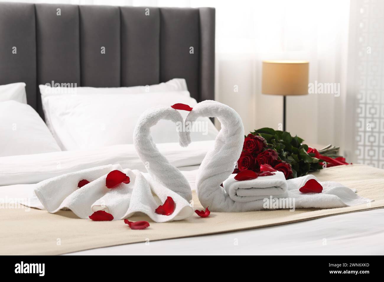 Luna di miele. Cigni fatti di asciugamani e bellissime rose rosse sul letto in camera Foto Stock