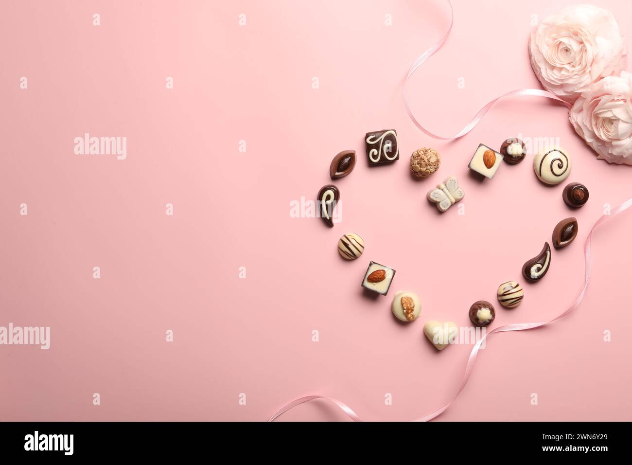 Cuore fatto con deliziose caramelle al cioccolato su sfondo rosa chiaro, piatto. Spazio per il testo Foto Stock