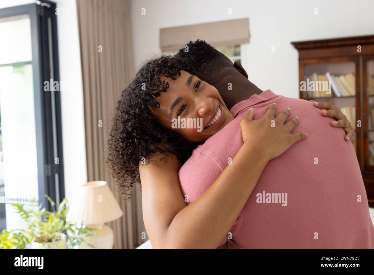 Una donna birazziale dai capelli ricci abbraccia un uomo afroamericano da dietro a casa Foto Stock Una donna birazziale dai capelli ricci abbraccia un uomo afroamericano da dietro a casa Foto Stock