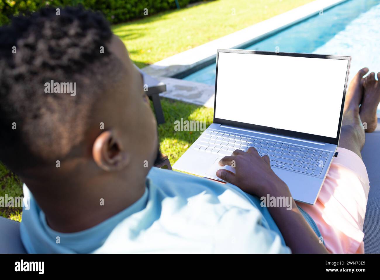 Un uomo afroamericano lavora su un laptop con uno schermo vuoto a bordo piscina Foto Stock