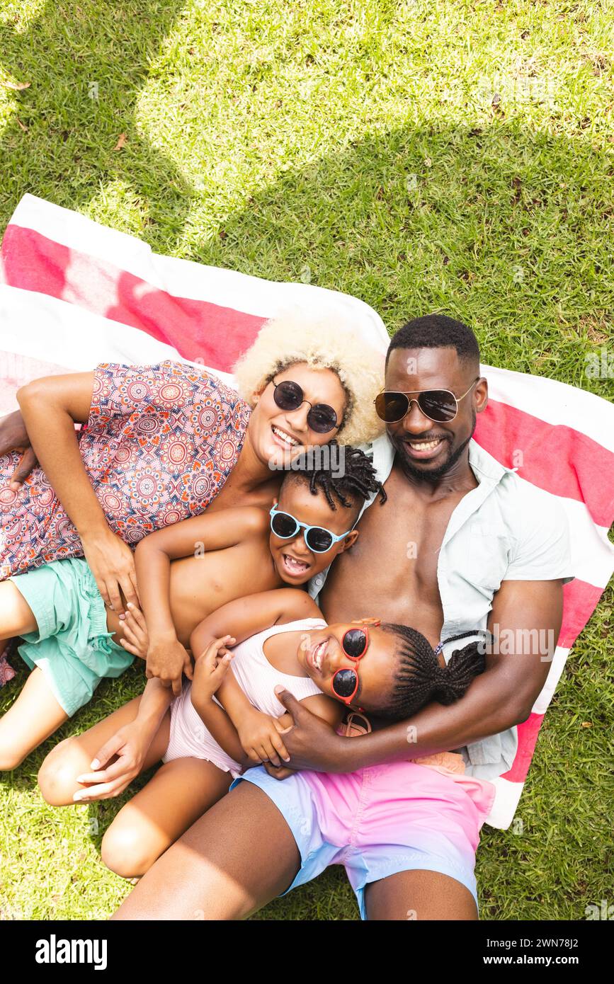 Una famiglia afroamericana giace su una coperta con due bambini, tutti sorridenti Foto Stock