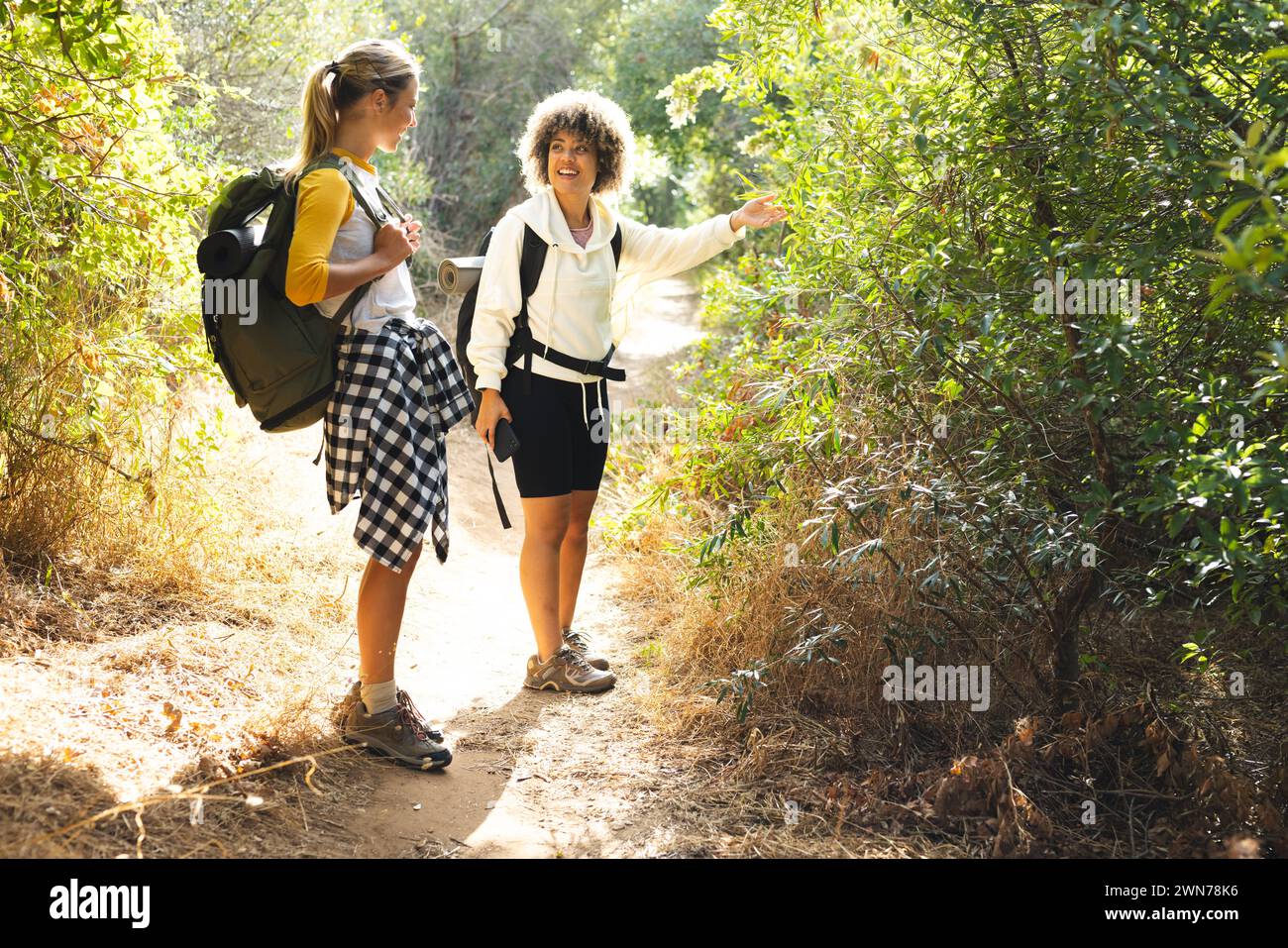 Giovane donna caucasica e donna birazziale stanno camminando su un sentiero soleggiato in un'escursione Foto Stock
